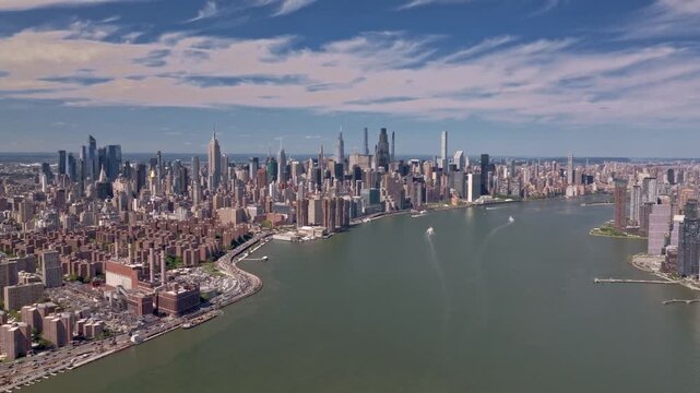This cinematic aerial shot captures the iconic New York City skyline as seen from high over the East River. The drone glides forward over the water, revealing the dynamic Manhattan cityscape.