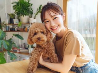 トリミングサロンで可愛いトイプードルを抱きしめる笑顔の女性ペットグルーミング
