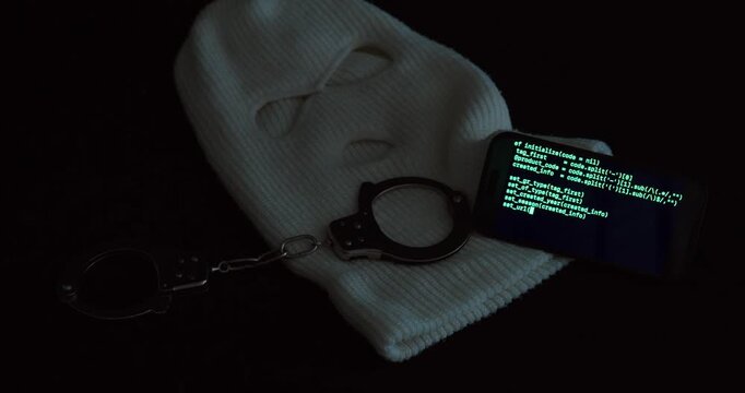 White mask, metal handcuffs, and smartphone with green AI code under red light. Symbolic scene for cybercrime, hacking, and digital investigation concepts.