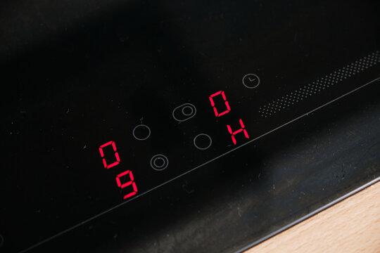 Close-up of a modern black glass cooktop control panel with red LED numeric display and touch buttons reflecting sleek kitchen appliance design and contemporary home interior.