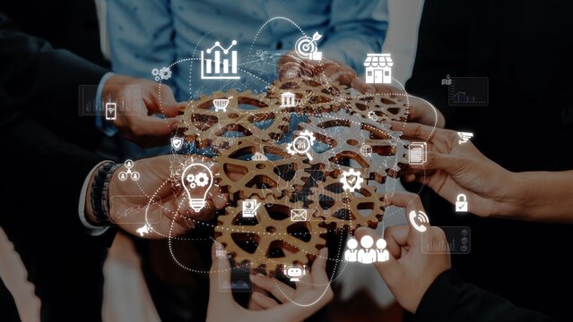 A diverse group of professionals holds a wooden gear symbolizing teamwork, surrounded by business icons showcasing innovation, strategy, and growth in a contemporary office. Raster