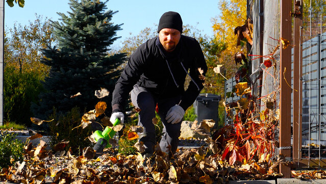 Autumn leaf raking. A man blows away piles of leaves with a leaf blower. 