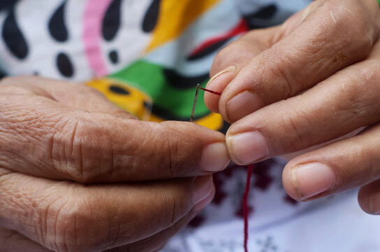 A skilled artisan carefully inserting threading into a needle to complete a beautiful floral design. Every stitch shows precision, dedication, and the art of creating something truly unique