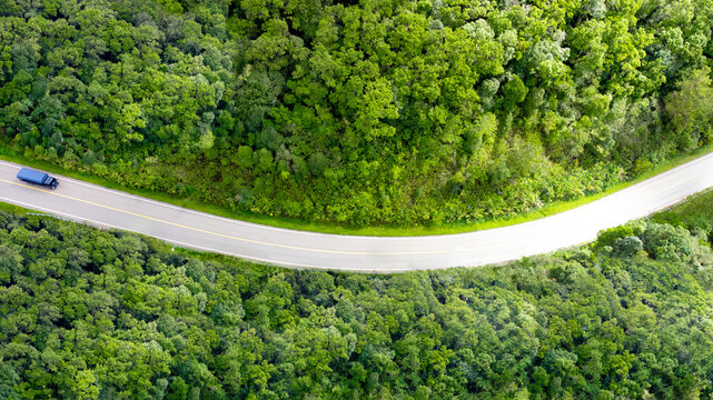 Concept of clean energy, environmental responsibility and smart mobility. Aerial view of a road through green forest for green logistics, eco transport and sustainable supply chain. Sustainable, ESG.