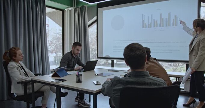 Business colleagues working together in a meeting using a projector screen. Discussing sales, charts, and bar graphs. - Powered by Adobe