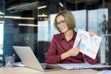 Businesswoman giving a financial presentation during a video call, confidently pointing at a chart while working remotely from a modern office using her laptop