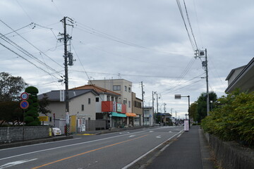 A street with a few buildings and a few cars. The street is empty and the sky is cloudy