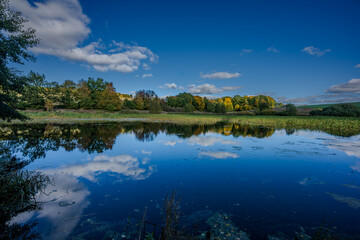 Sch&ouml;ner Herbsttag mit klar reflektierenden Wolken &uuml;ber einem ruhigen Gew&auml;sser in der Natur