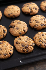 Baked chocolate chip cookies on a black baking tray