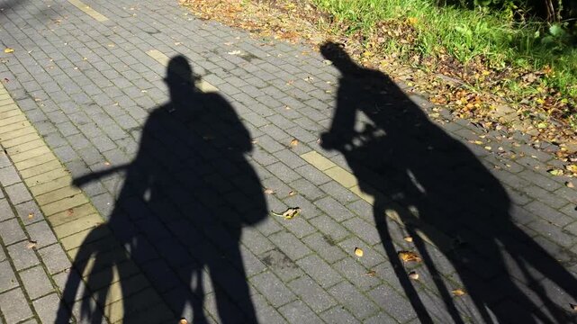 Shadows of cyclists. A couple rides along a bike path, only shadows visible.