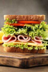 Tasty sandwich with ham, cheese and vegetables on wooden table, closeup