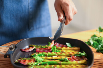 Man adding onion into pan with grilled vegetables at table indoors, closeup