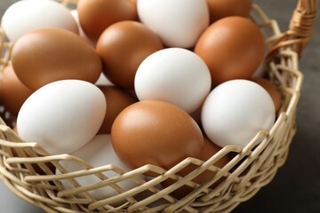 Raw chicken eggs in wicker basket on grey table, closeup