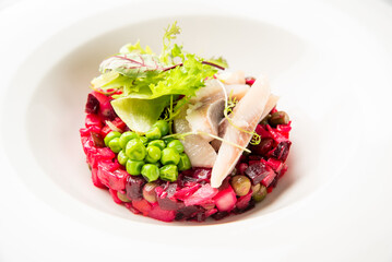 Gourmet beet and potato salad with pickled herring, green peas, fresh greens, and lime wedge, artistically plated on a white dish. Top-down view, vibrant colors, fine dining style.