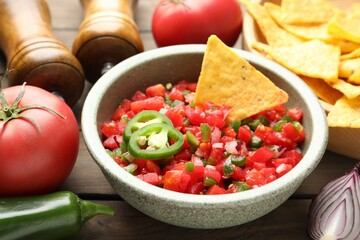 Tasty salsa with nachos and ingredients on wooden table, closeup