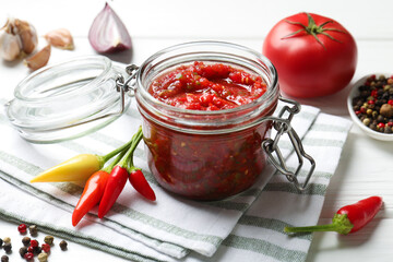Tasty salsa sauce in jar and ingredients on white wooden table, closeup