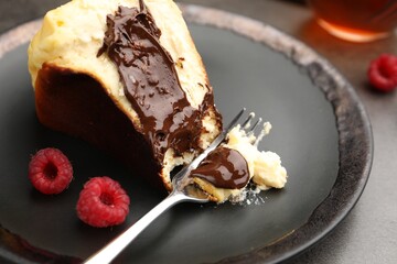 Piece of delicious Basque cheesecake with chocolate sauce and raspberries on grey table, closeup