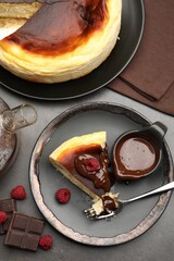 Delicious Basque cheesecake with chocolate sauce and raspberries on grey table, flat lay
