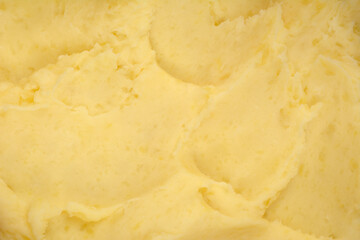 A detailed horizontal close-up shot of creamy, pale yellow mashed potatoes showing a soft, textured...