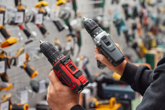 Close-up of a person holding two cordless drills in a hardware store. Concept of construction, repair, and tool selection for home improvement or professional use.