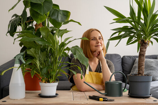 Woman caring for indoor green plants at home with watering tools