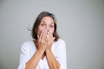 Mature woman with hand covering mouth smiling in studio portrait