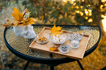Outdoor glass table setup featuring a skull adorned with autumn leaves next to a wooden tray filled with assorted supplements. Mortality and health awareness in autumn visuals, memento mori,
