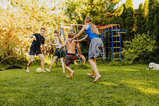 Teens and children playing football together in backyard on summer day