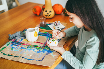 Female kid painting a pumpkin on a cup for an halloween party fest - Holidays and art concept - Main focus on hands