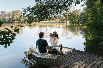 Couple enjoying picnic and photography together by the lakeside outdoors