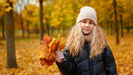 girl with fall leaves in park, wearing cozy sweater and hat, enjoying vibrant autumn colors. ideal...