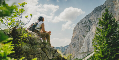 Young woman hiker resting on rock with mountain view during trekking in nature