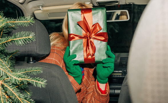 Woman holding Christmas gift in car with tree preparing for holiday