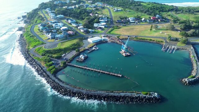 Drone aerial landscape of crane and rocky pier break wall with local town suburbs at Crowdy Head boat harbour wharf located along scenic Australian coastline headland with ocean waves travel tourism