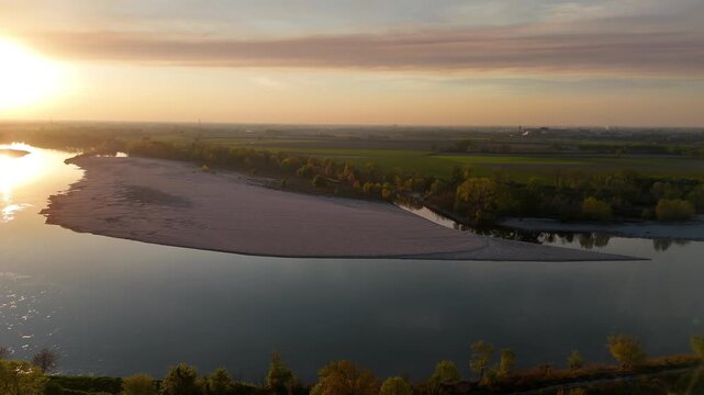 Golden-hour view of the River Po from Olza, Italy, with a sandbar midstream and warm light illuminating the water and surrounding rural landscape in Lombardy.
