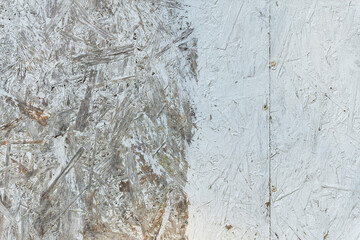 A close-up of a wall made of compressed wood chips. The surface of the wood has turned gray with age. Half of the surface is painted white. The joints between the sheets are visible. Background.
