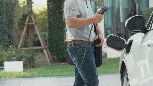 A man unplugs the electric vehicle's charger at his residence. Concept of the use of electric vehicles in a progressive lifestyle contributes to a clean and healthy environment.