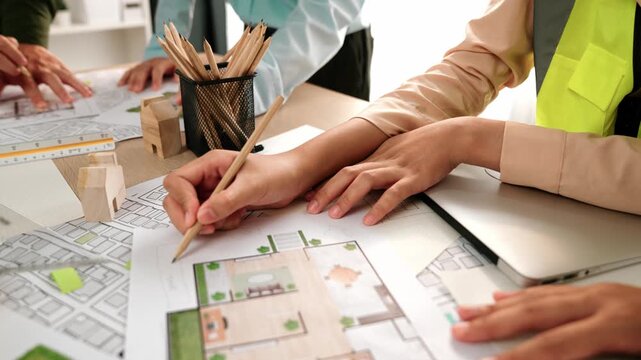 Smart architect and safety engineer discussion about building blueprint on table with architectural document, measurement tools and wooden block scatter around at modern office. Closeup. Delineation.
