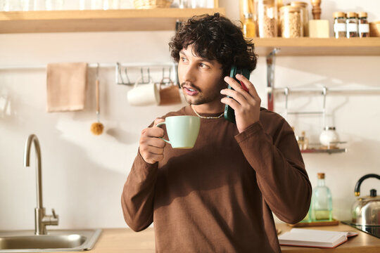 Handsome young man enjoys coffee while talking on the phone in a stylish kitchen setting