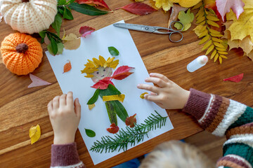 Sweet child, boy, applying leaves using glue while doing arts and crafts at home