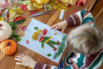 Sweet child, boy, applying leaves using glue while doing arts and crafts at home