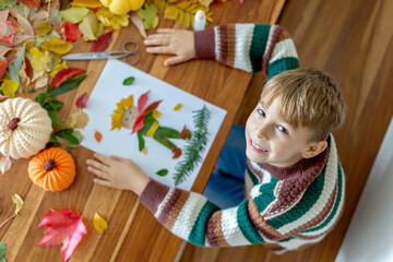 Sweet child, boy, applying leaves using glue while doing arts and crafts at home