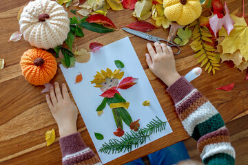 Sweet child, boy, applying leaves using glue while doing arts and crafts at home