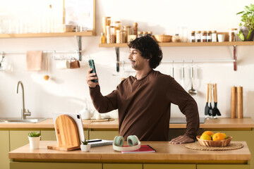 Young man enjoying a moment in the stylish kitchen while using his smartphone