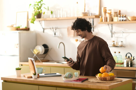 Young handsome man enjoys a moment in a bright kitchen while checking his phone