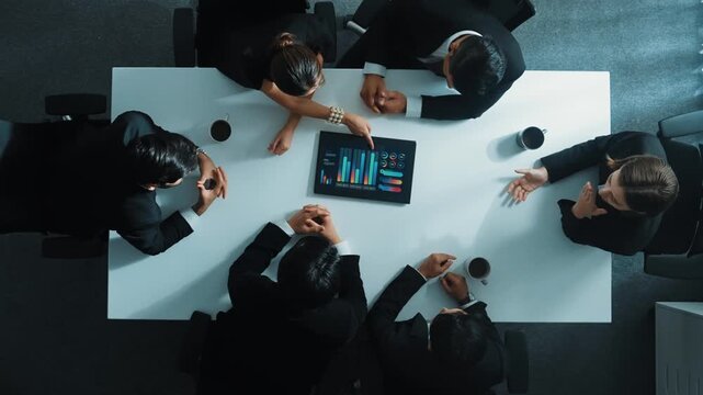 Top down aerial view of professional businessman analyze stock market chart with tablet with investment graph placed at table while investor group pointing at tablet. Creative business. Directorate.