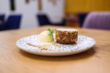 Chocolate lava cake with vanilla ice cream, crushed nuts and powdered sugar, artistically plated on dotted ceramic plate on wooden table in cozy restaurant.