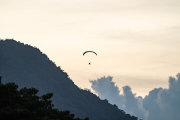 Paramotor flying over tropical mountain ridge at sunset