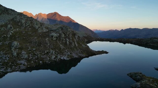 Aerial view of the serene lake reflecting the majestic mountains under the soft glow of dawn, creating a tranquil landscape, Medel (Lucmagn), Graub&uuml;nden, Switzerland.