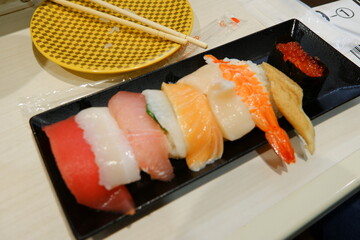 A plate of assorted fresh nigiri sushi, including tuna, salmon, and shrimp, served at a Japanese conveyor belt sushi restaurant